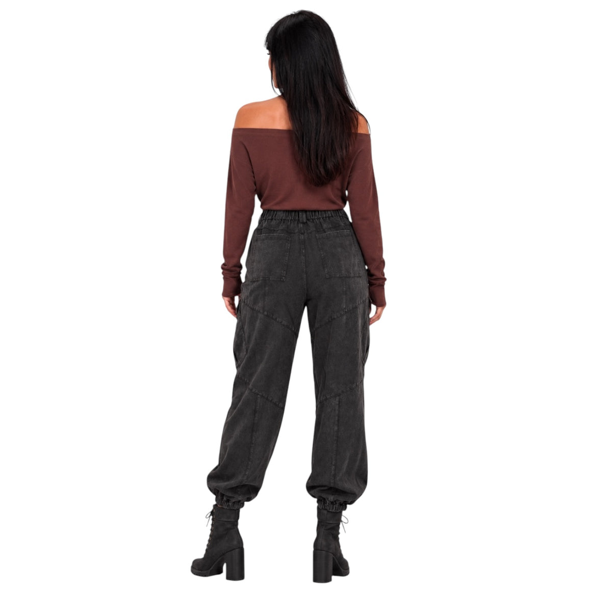 A woman shown from the back wearing a brown off-the-shoulder long-sleeve top, dark gray baggy high-waisted pants, and black lace-up ankle boots, set against a plain white background.