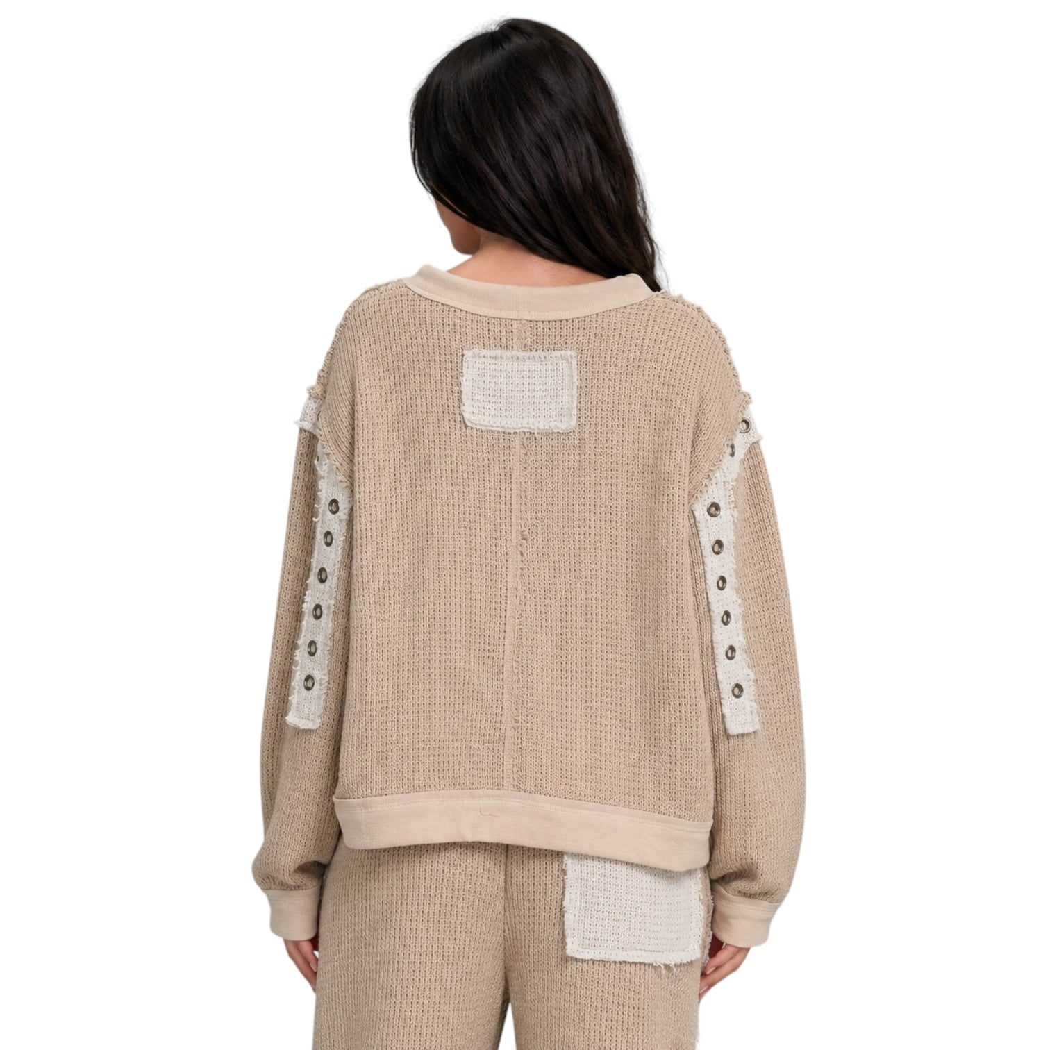 A person shown from the back wearing a beige textured knit sweater and matching pants with contrasting cream patchwork details and decorative buttons on the sleeves, against a plain white background.