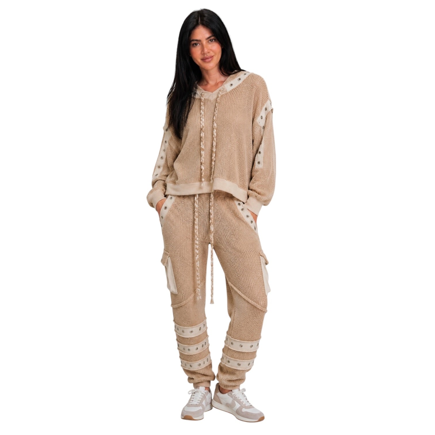 A woman modeling a beige knit loungewear set consisting of a cropped hoodie and matching cargo joggers, styled with white sneakers against a plain white background.