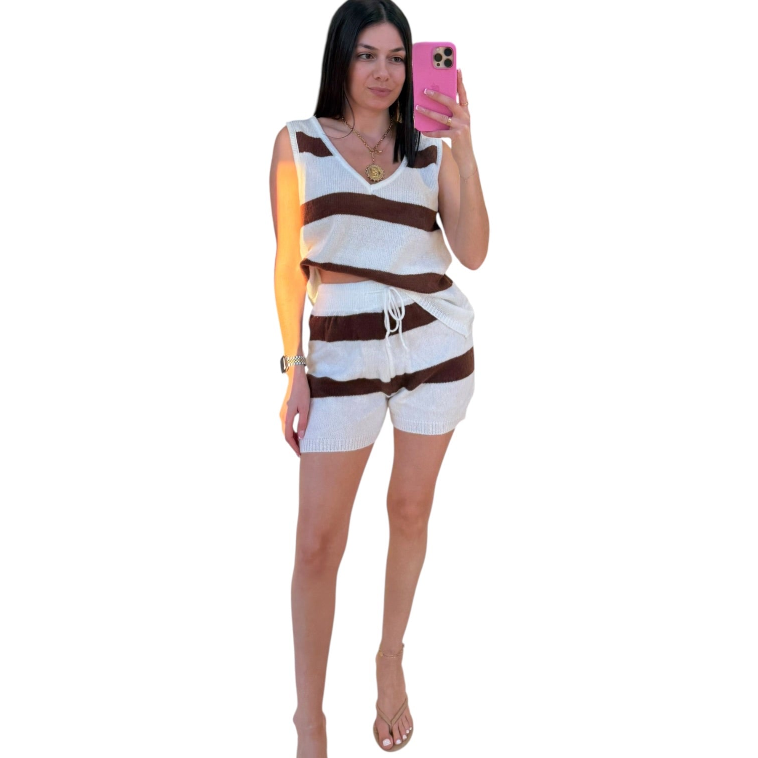 Woman taking a mirror selfie wearing a sleeveless striped top and shorts on a white background