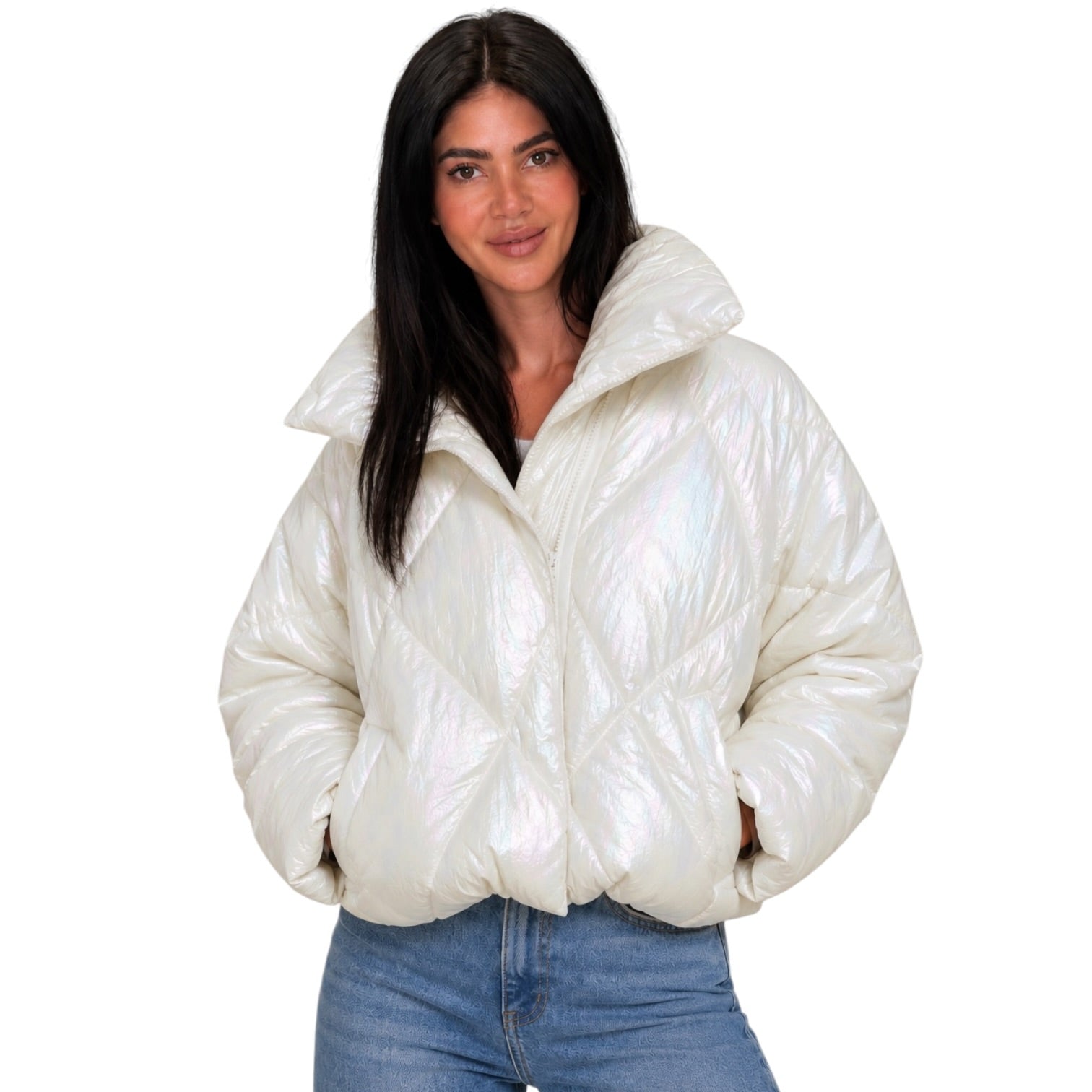 A woman modeling a shiny, puffer-style cropped jacket in a metallic cream or off-white color, paired with blue jeans, against a plain white background.