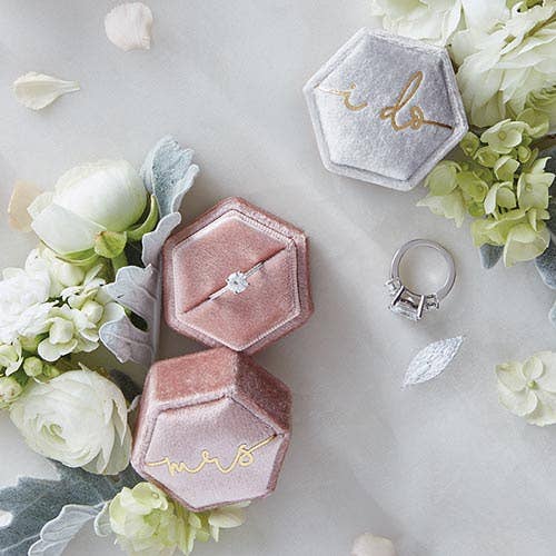 Hexagonal velvet ring boxes with 'Mr.' and 'Mrs.' on a marble surface with flowers.