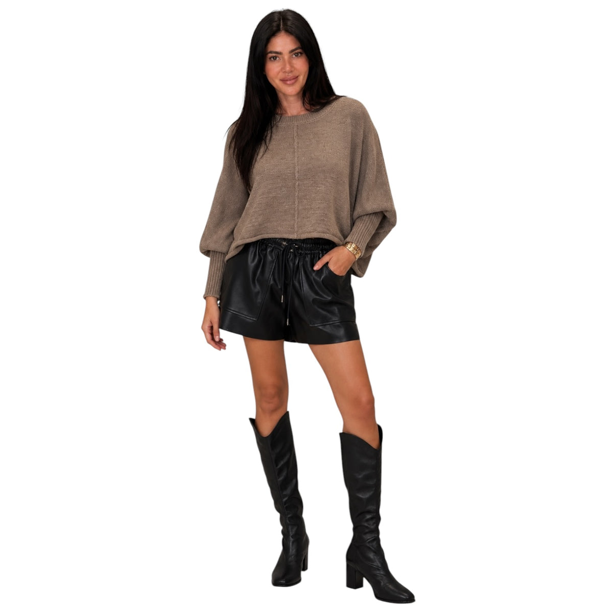 A woman modeling a taupe knit long-sleeve crop top, black faux-leather shorts, and black knee-high boots against a plain white background.