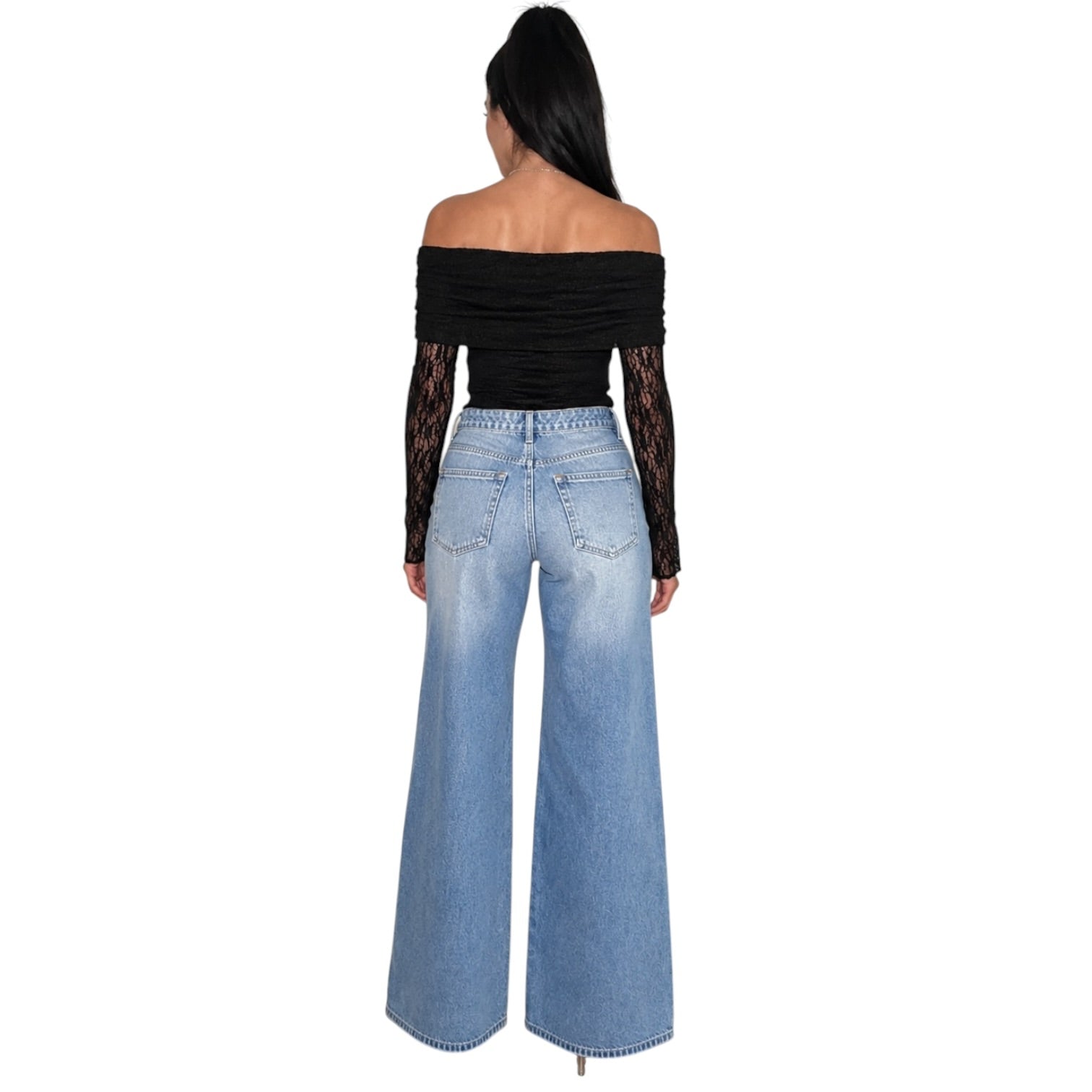 A woman shown from the back wearing a black off-the-shoulder bodysuit with sheer black lace sleeves and high-waisted, wide-leg light blue denim jeans, set against a plain white background.