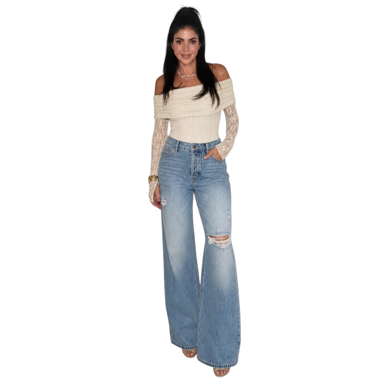 A woman modeling a cream off-the-shoulder knit top with long lace sleeves and light-wash blue wide-leg distressed jeans, shown against a plain white background.