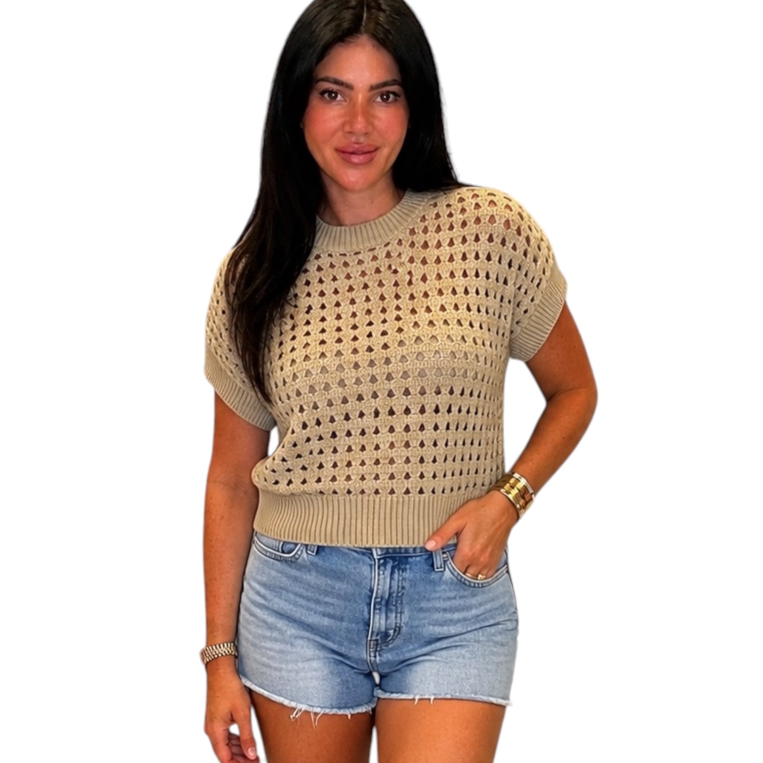 Woman wearing a beige crochet top and denim shorts on a white background