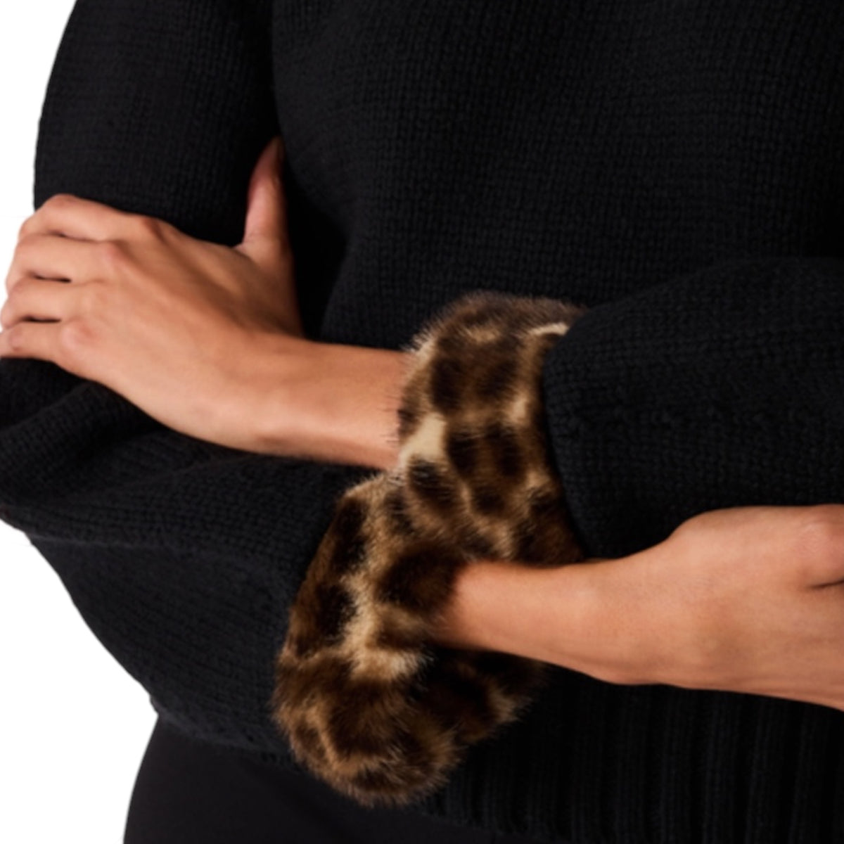Close-up of a person wearing a black ribbed knit sweater with a brown and black leopard-print faux fur cuff on the sleeve.