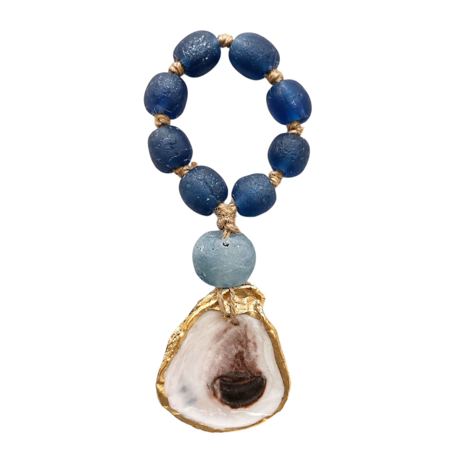 A beaded necklace featuring dark blue textured glass beads, a light blue stone bead, and a large natural oyster shell pendant with gold-toned metal trim, shown on a plain white background.