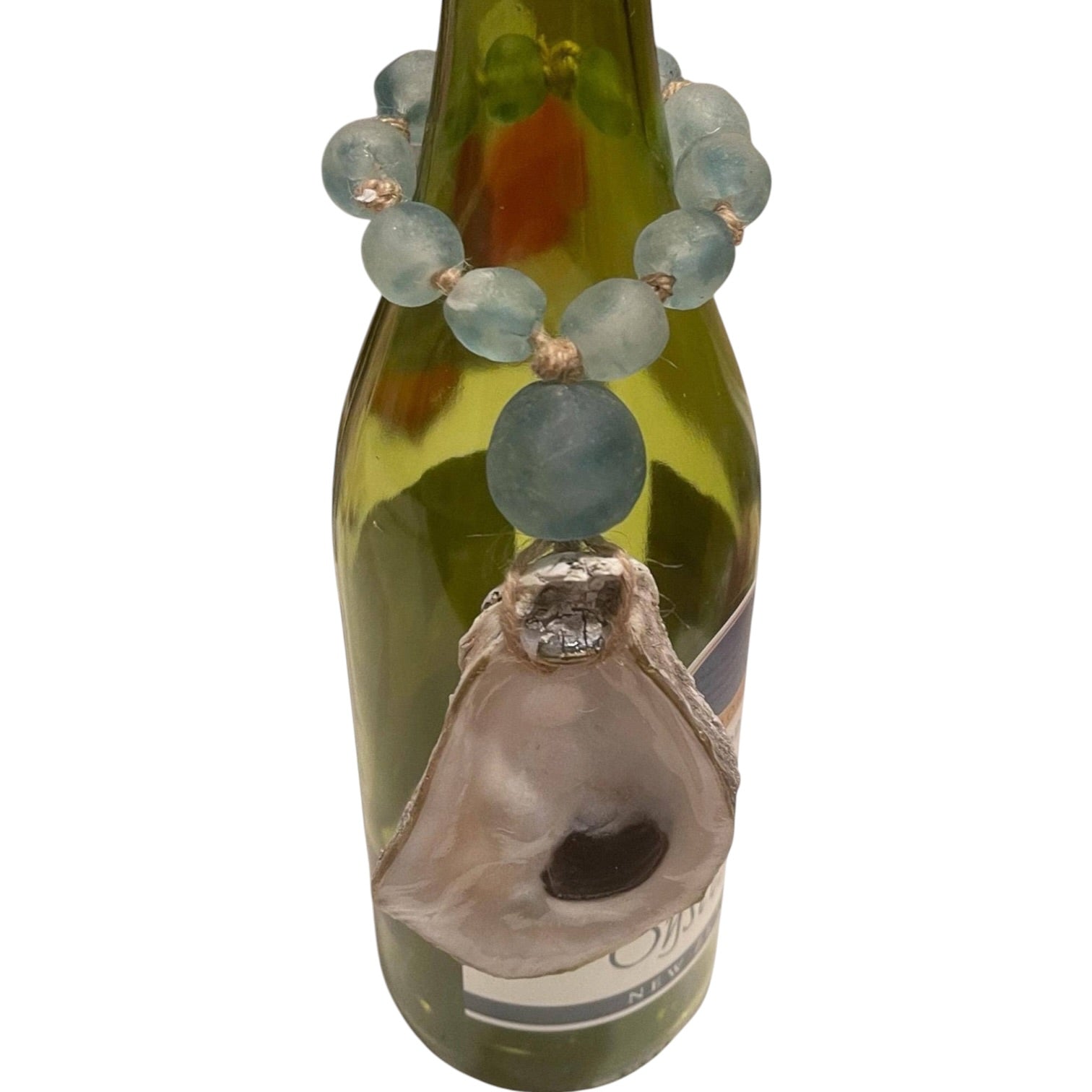 A beaded necklace with light blue-green round beads and a large natural oyster shell pendant, displayed on a green glass bottle against a white background.