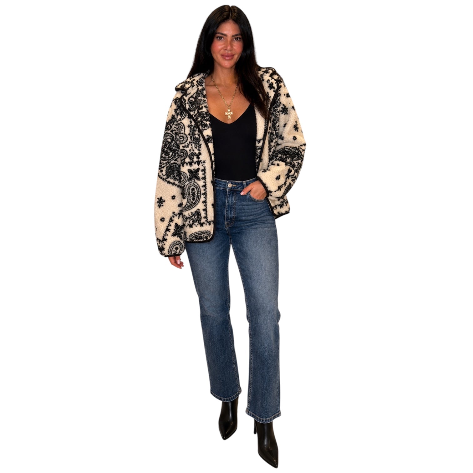 A woman modeling a black and beige paisley patterned open-front jacket over a black top and blue jeans, standing against a plain white background.