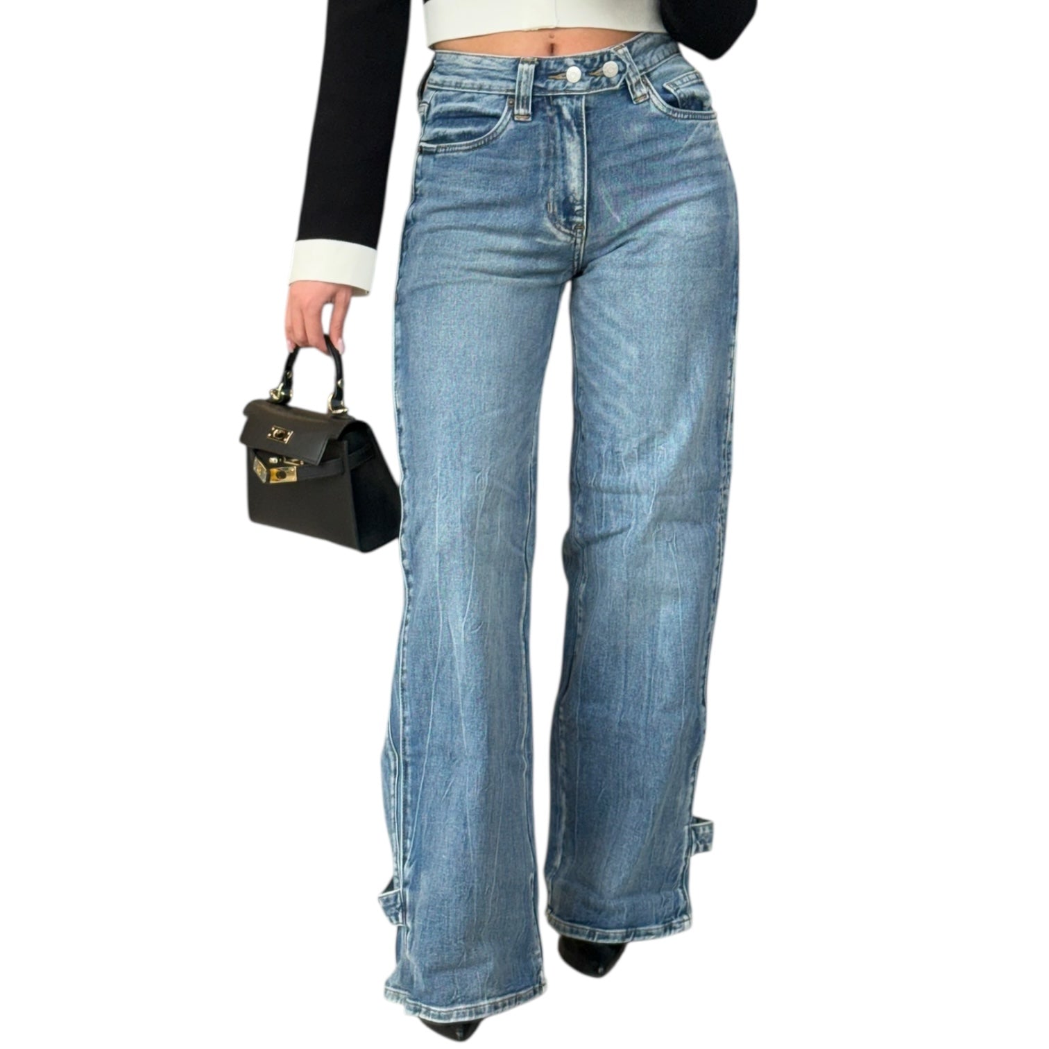Person wearing blue jeans holding a black handbag on a white background