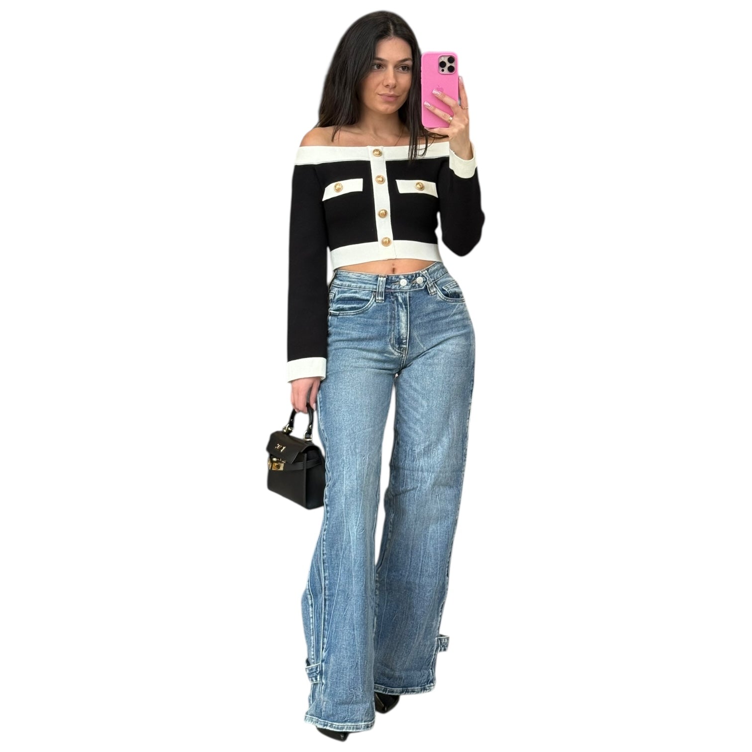 Woman wearing a black and white off-shoulder top with blue jeans, holding a phone and a handbag.