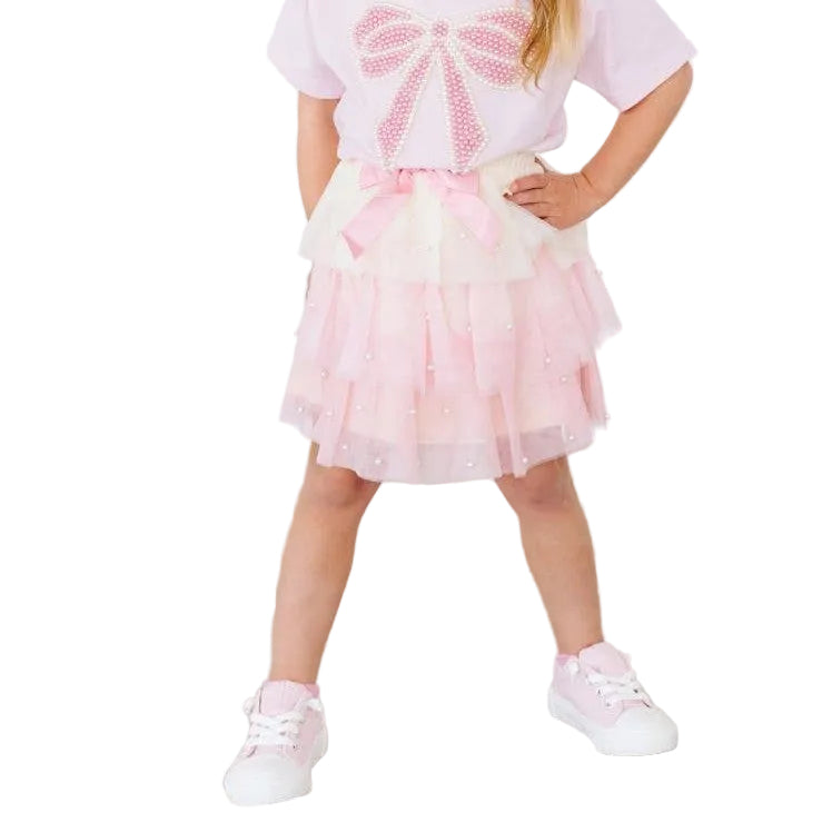 Young girl wearing a pink dress with a bow design on a wooden floor.