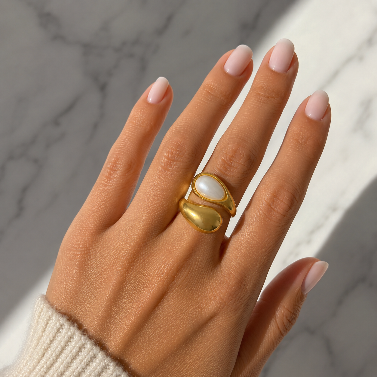 Hand wearing a gold ring with a large gemstone on a marble background