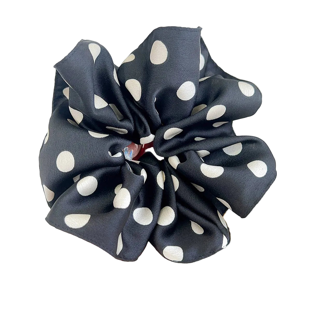 Black scrunchie with white polka dots held by a hand against a light background
