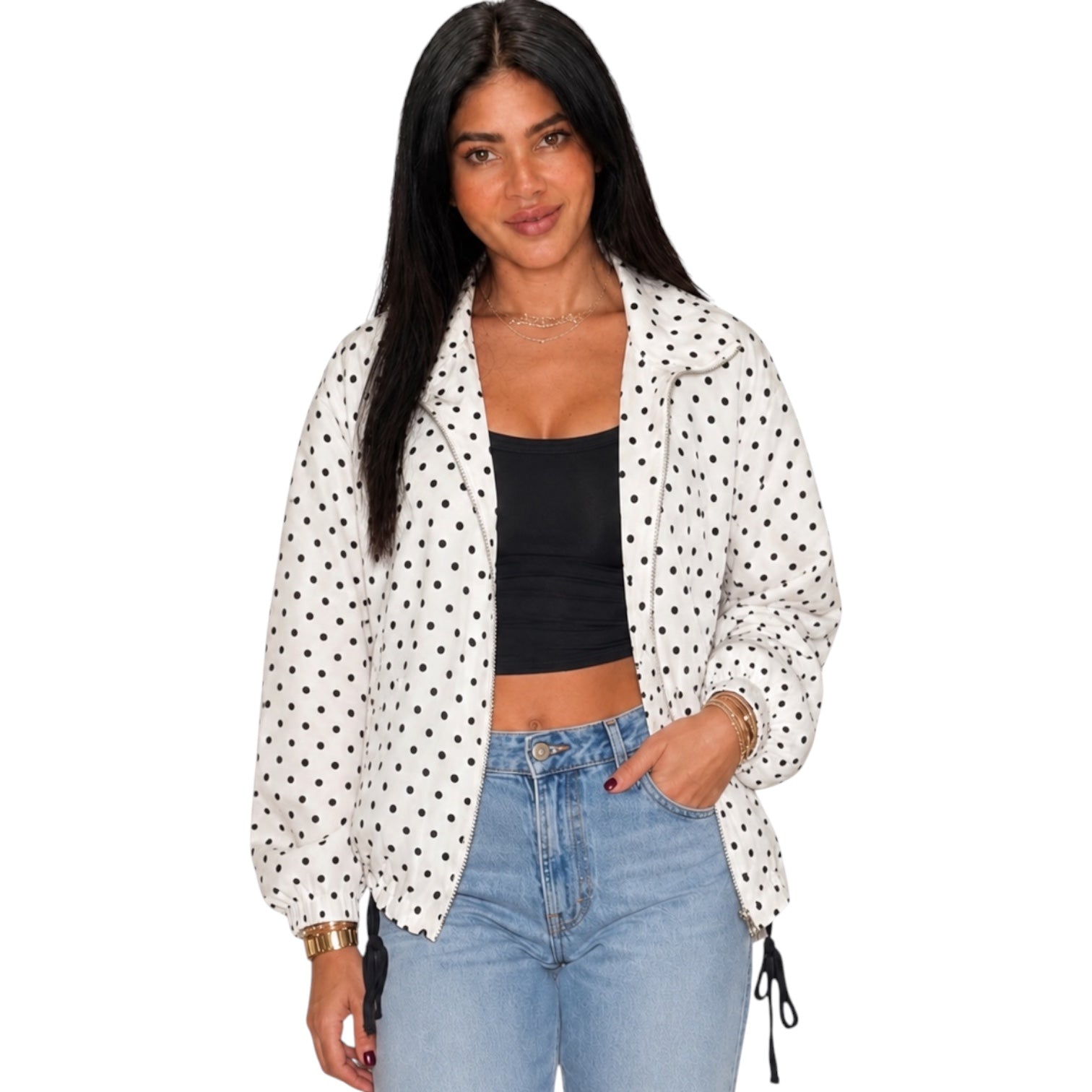 A woman modeling a white lightweight jacket with black polka dots, worn open over a black crop top and light blue jeans, against a plain white background.