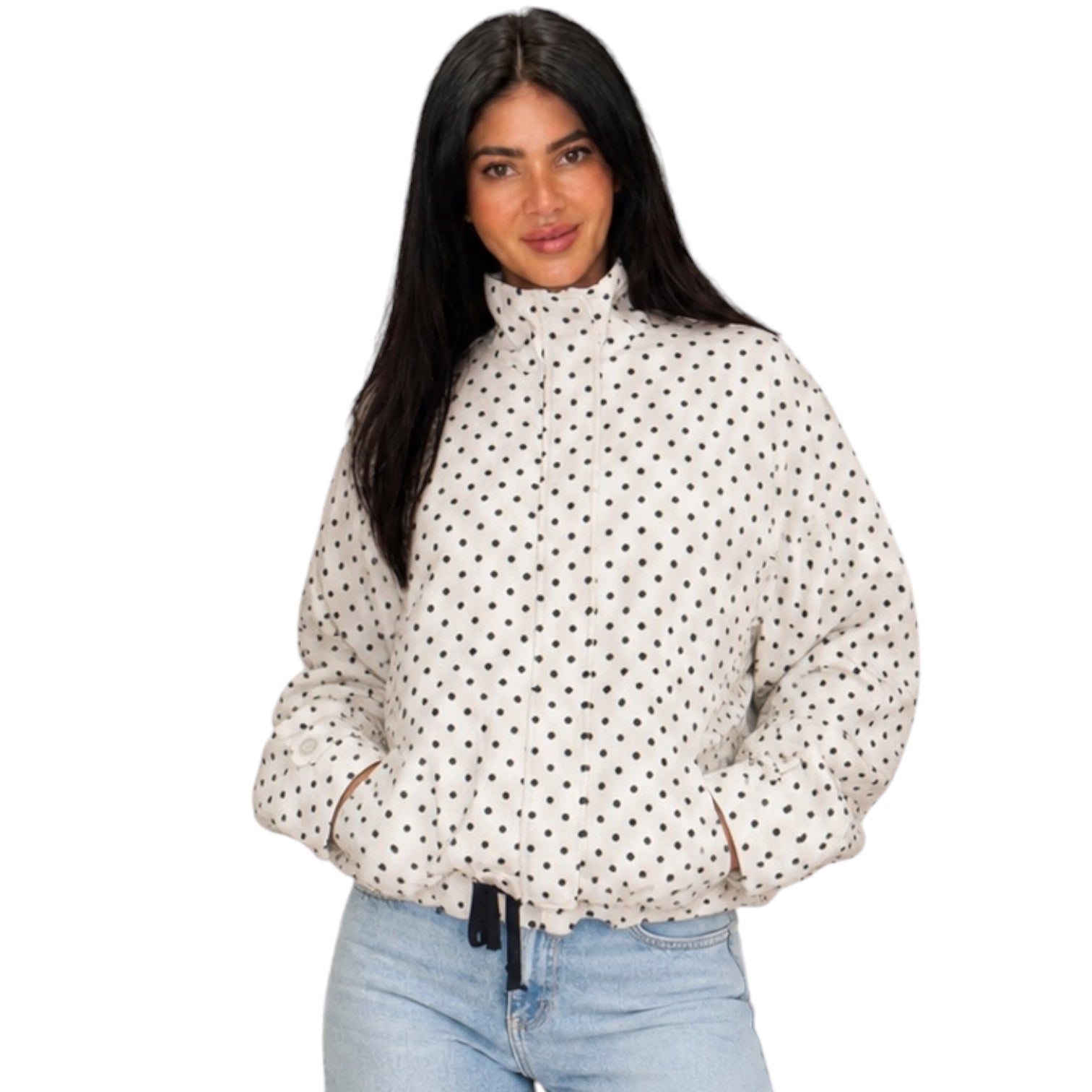 A woman wearing a cream-colored puffer jacket with a black polka dot pattern and light blue jeans, photographed against a solid white background.
