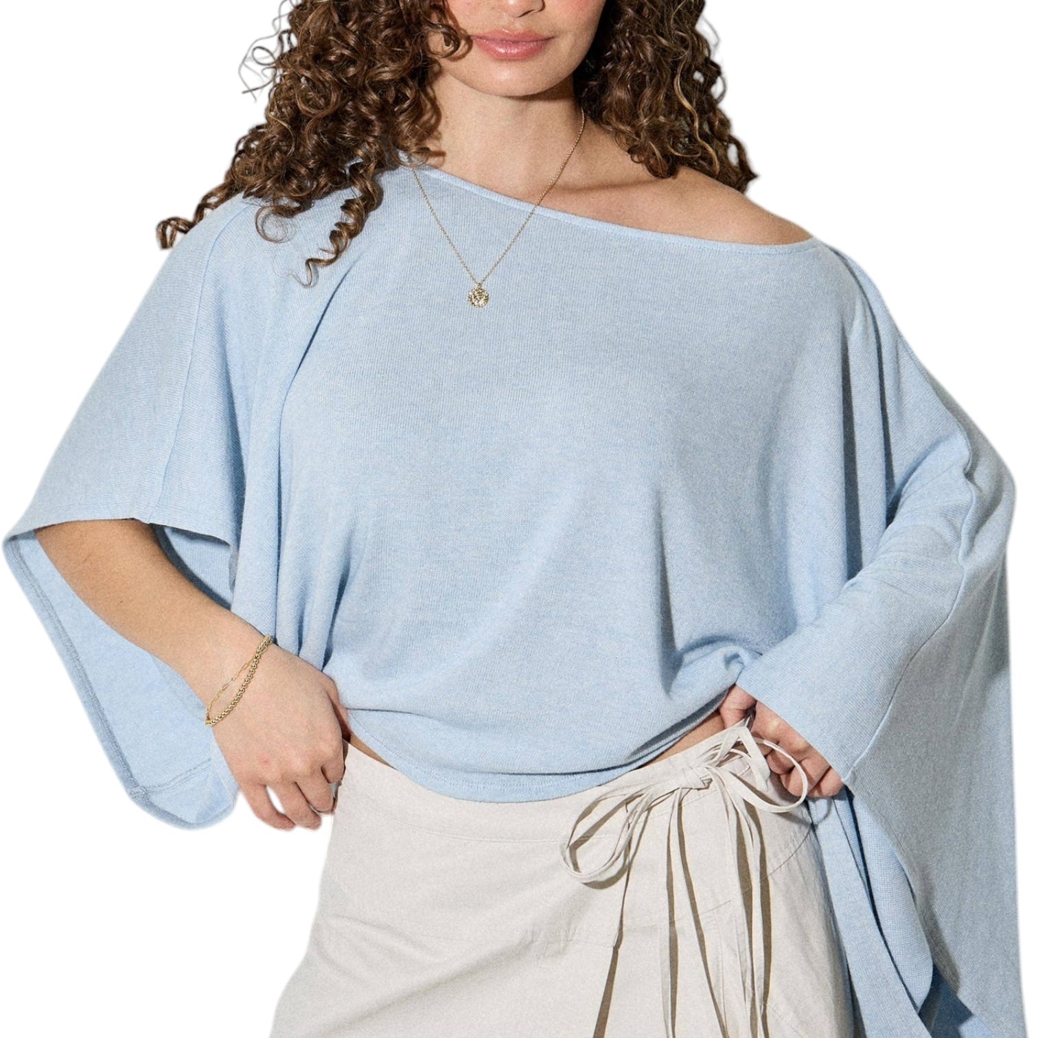 Woman wearing a light blue off-shoulder top with beige pants on a white background