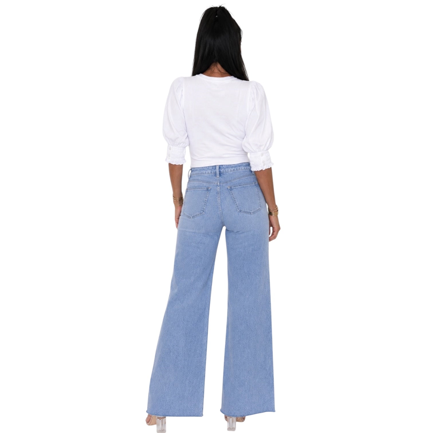 A woman shown from the back wearing a white puff-sleeve top and light blue wide-leg jeans against a plain white background.