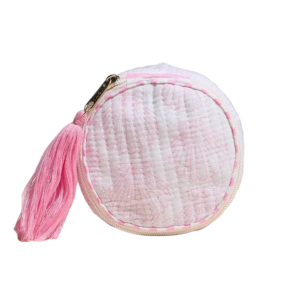 Round pink and white textured pouch with a tassel on a beige surface and blue background