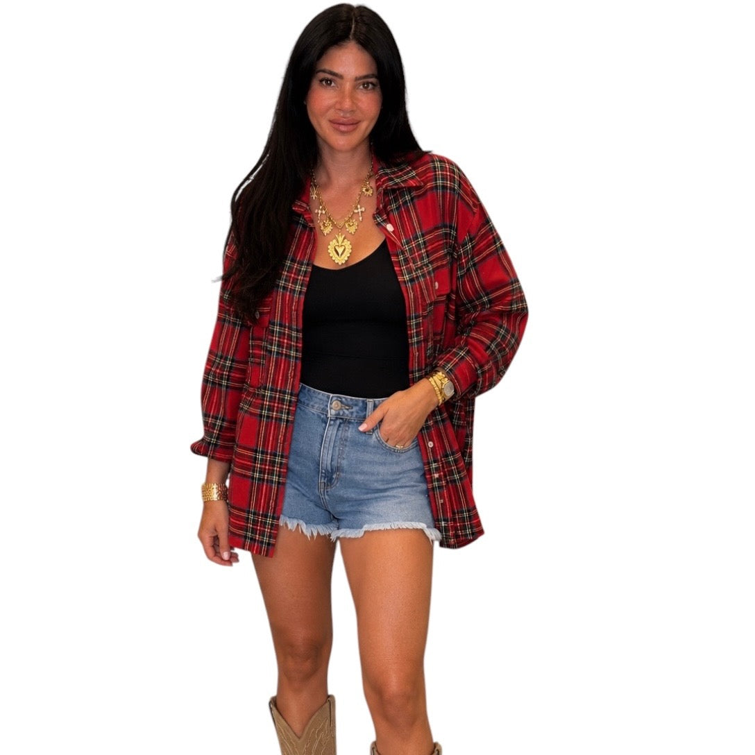 A woman modeling a red and black plaid flannel shirt over a black tank top and denim shorts, standing against a plain white background.