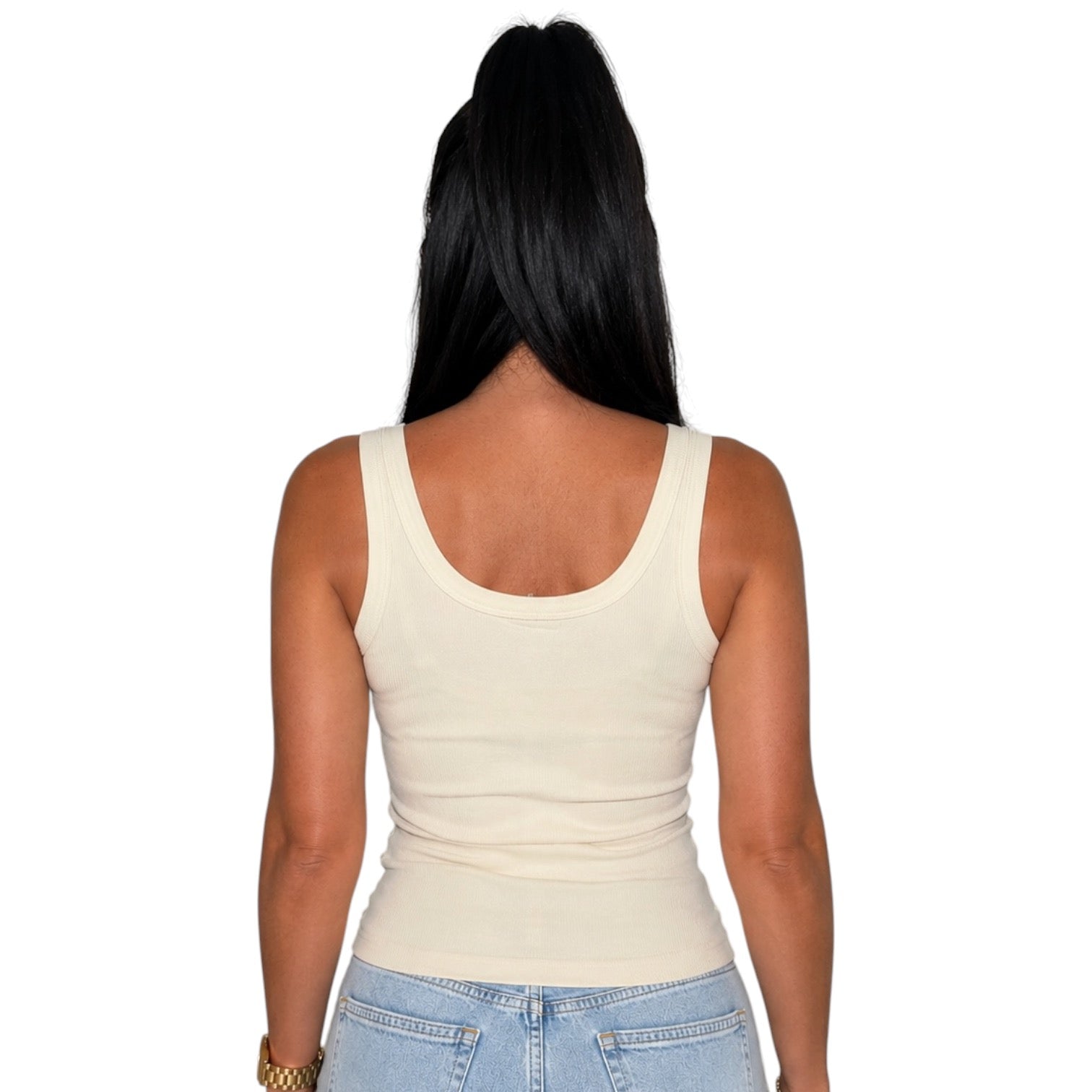 A woman viewed from the back wearing a fitted scoop-neck tank top in a light cream color, paired with light blue jeans, against a plain white background.