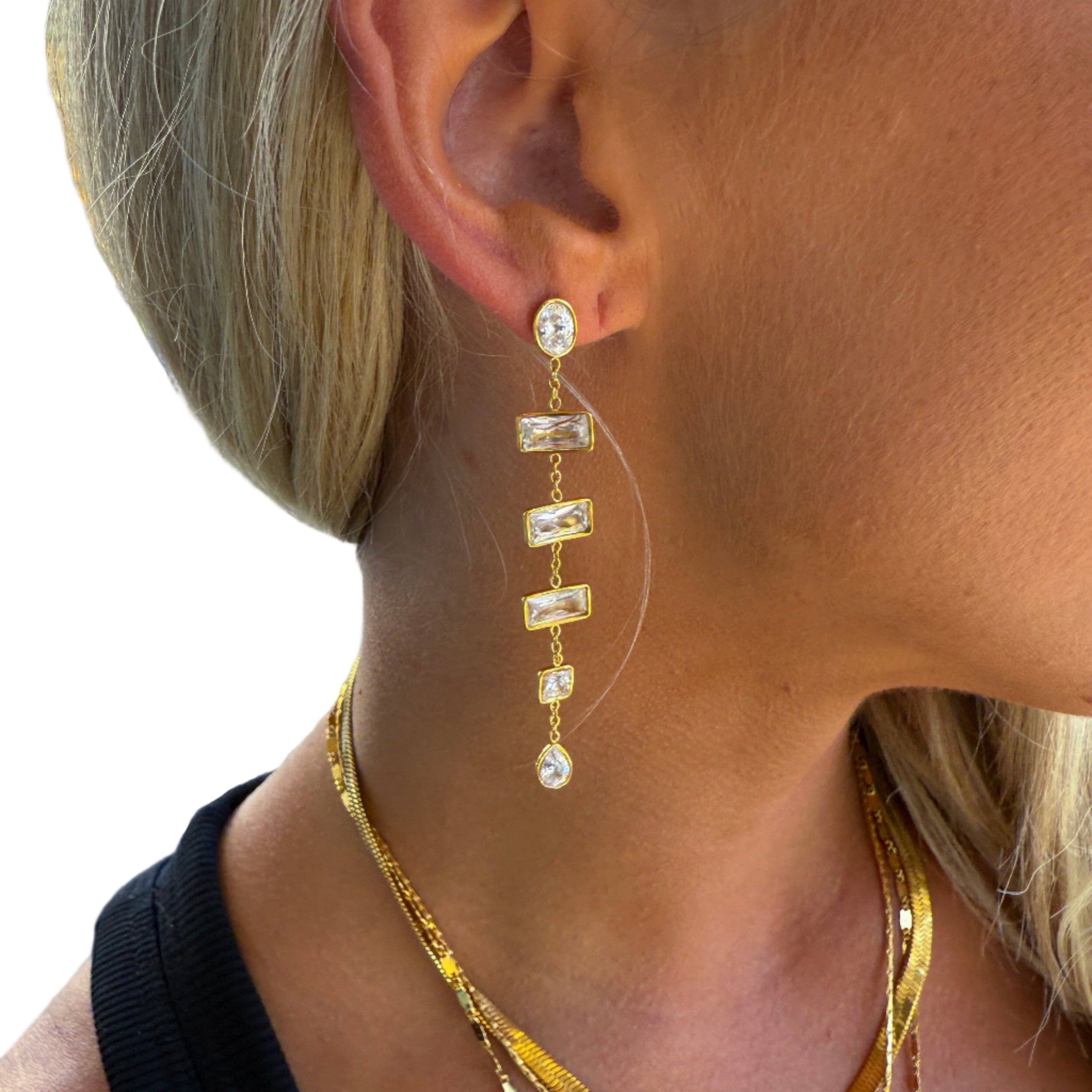 Close-up of a person wearing gold earrings and necklaces with a blurred outdoor background.
