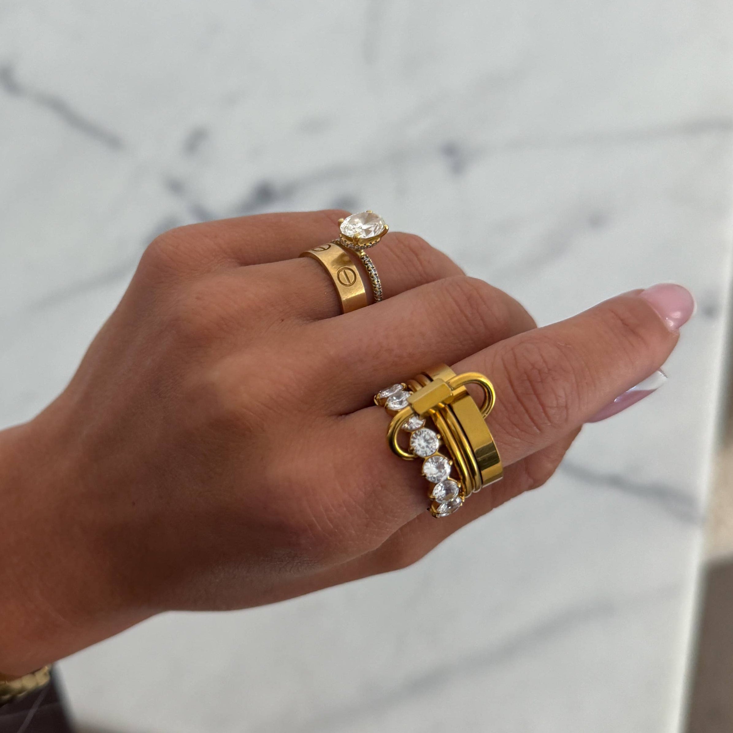 Hand wearing multiple gold rings with gemstones on a neutral background