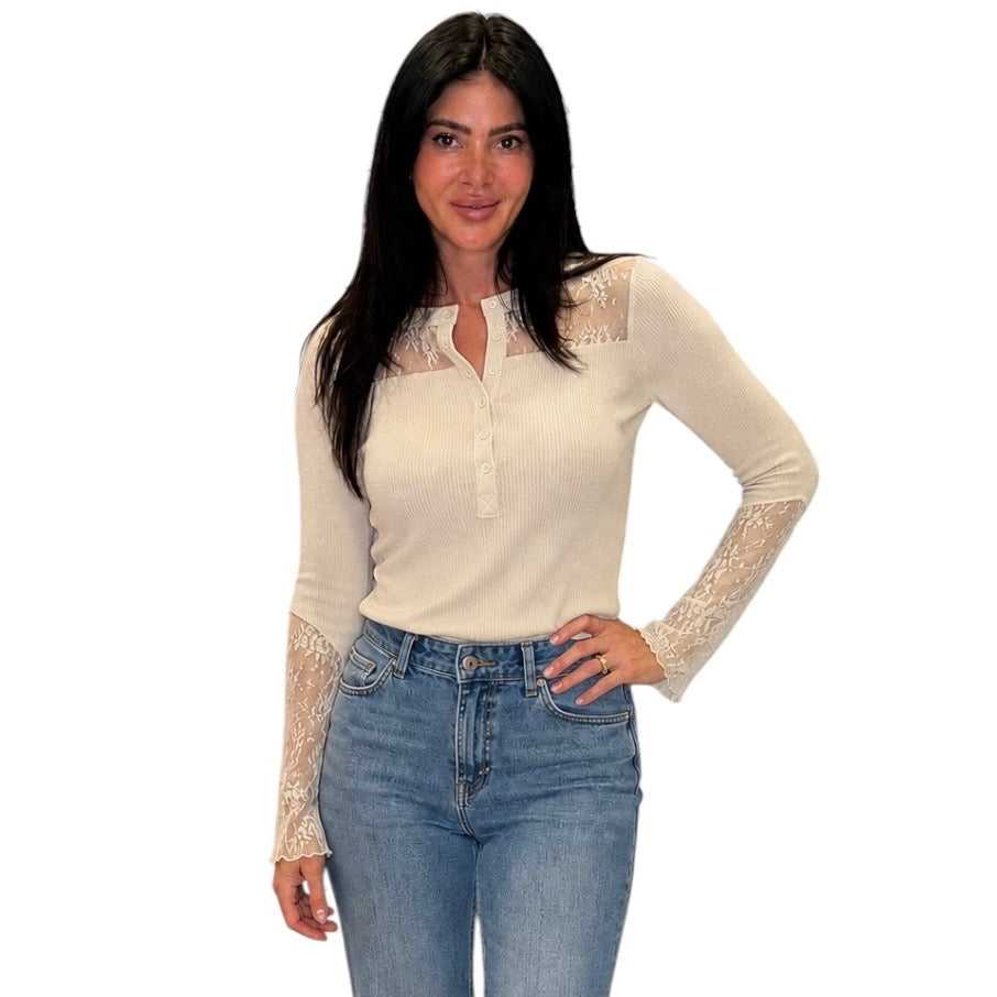 A woman modeling a cream ribbed long-sleeve top with lace panels on the chest and sleeves, paired with blue jeans, against a plain white background.