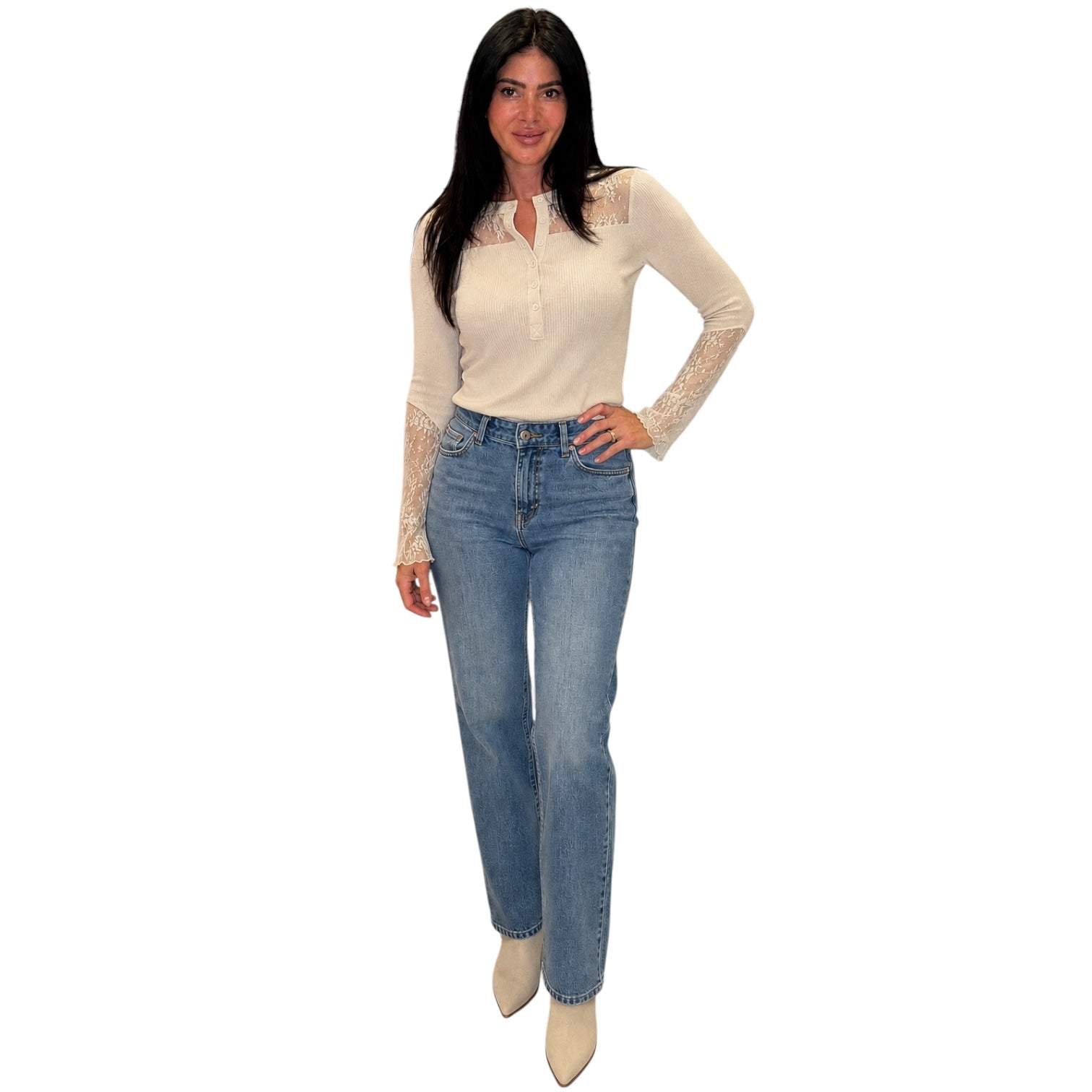 A woman modeling a cream long-sleeve top with lace detailing on the chest and sleeves, paired with light-wash blue jeans and beige ankle boots, against a plain white background.