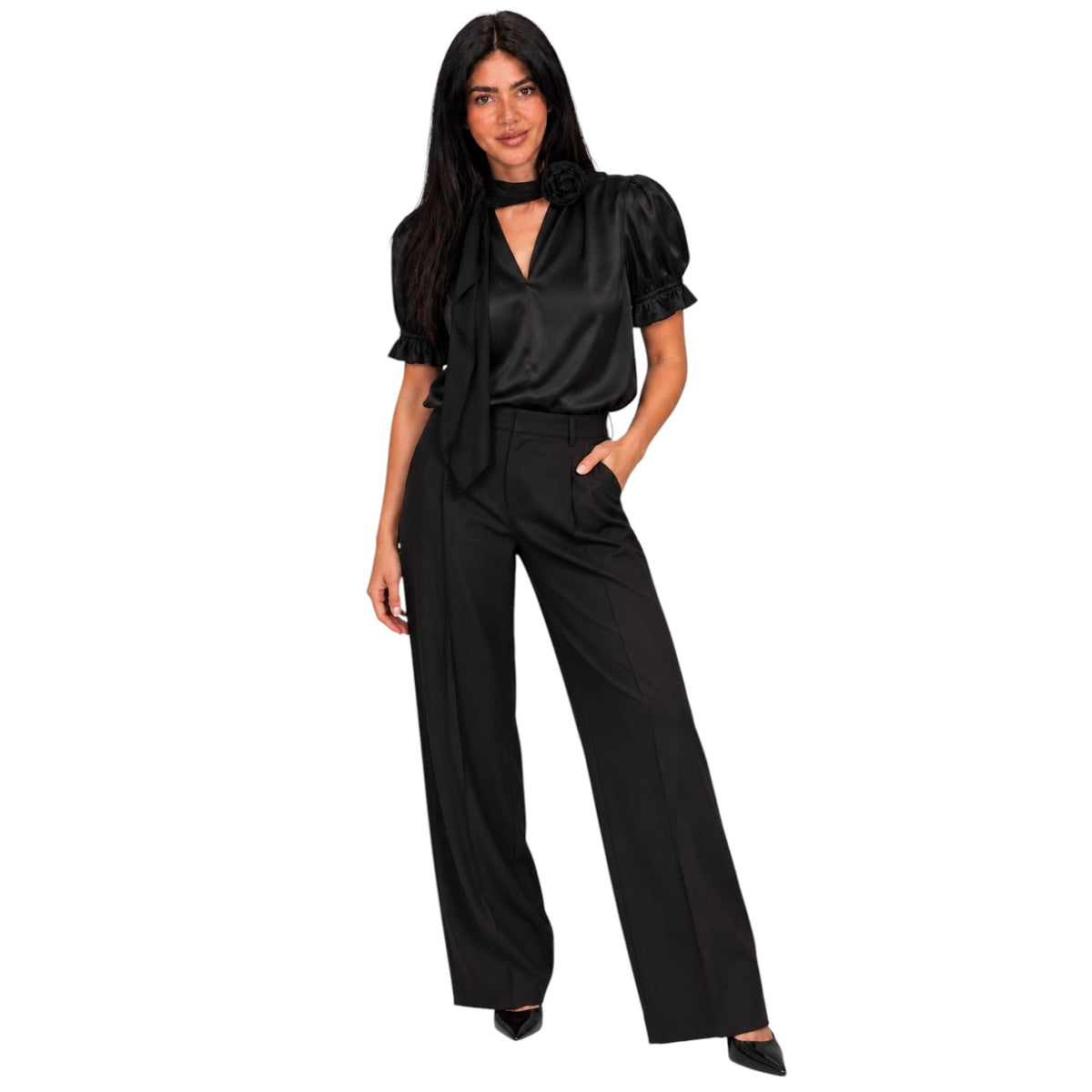 A woman modeling a black satin short-sleeve blouse with puff sleeves and a keyhole cutout, paired with black wide-leg trousers and black pointed heels, against a plain white background.