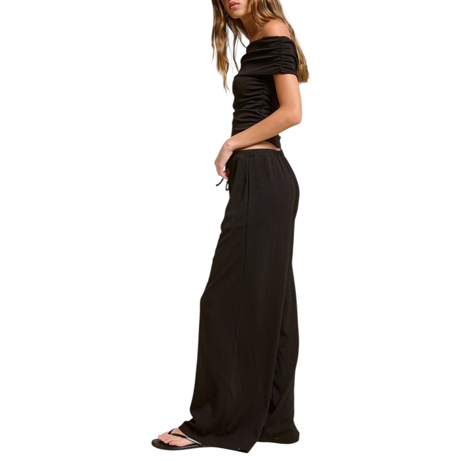 Woman wearing a black off-shoulder top and wide-leg pants on a white background