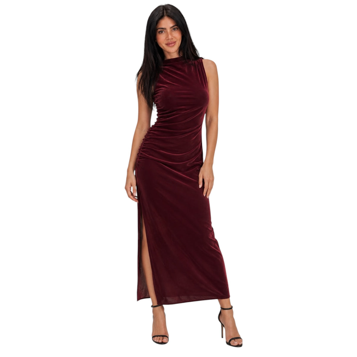 A woman modeling a sleeveless, high-neck, floor-length burgundy velvet dress with ruching and a thigh-high slit, paired with black high-heeled sandals, set against a plain white background.