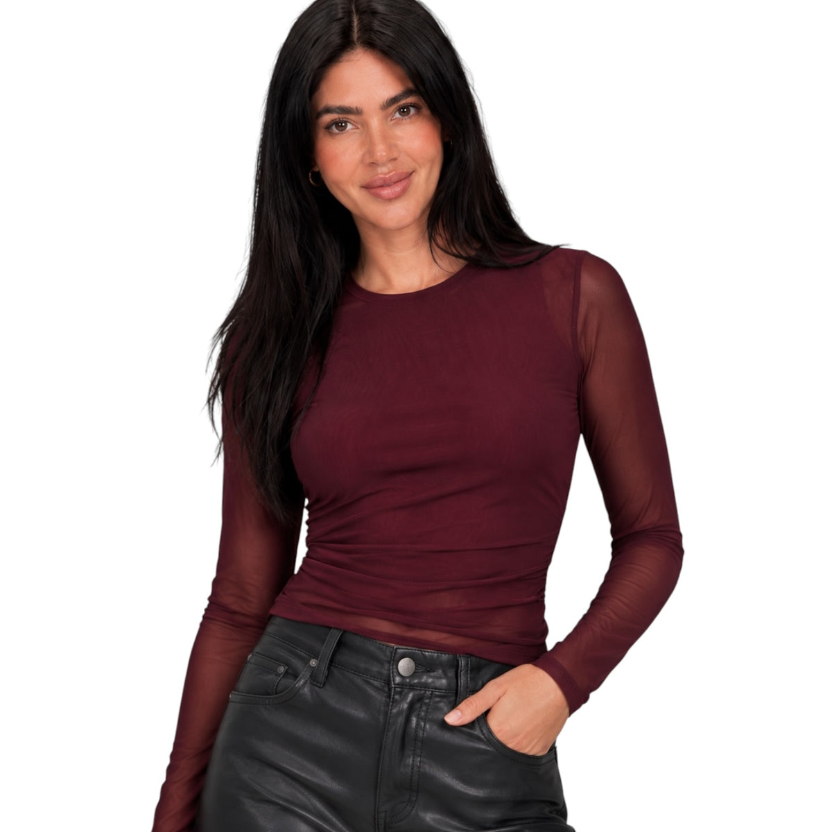 A woman modeling a fitted long-sleeve top with sheer mesh sleeves in a deep burgundy color, paired with black leather-look pants, against a plain white background.