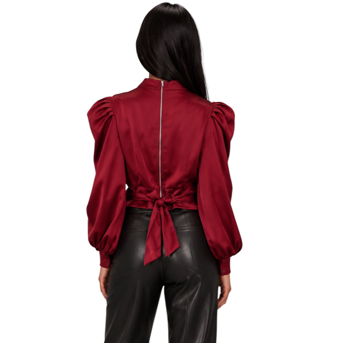 A woman shown from the back wearing a deep red satin blouse with dramatic puffed sleeves, a high neckline, and a tie detail at the waist, paired with black faux-leather pants against a plain white background.