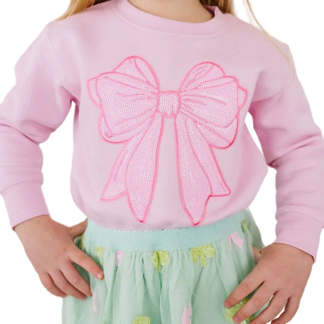 Child wearing a pink sweatshirt with a large bow design on a plain background