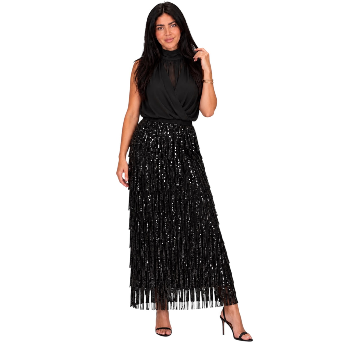 A woman modeling a sleeveless black high-neck top and a long black sequined fringe maxi skirt, paired with black high-heeled sandals, against a plain white background.