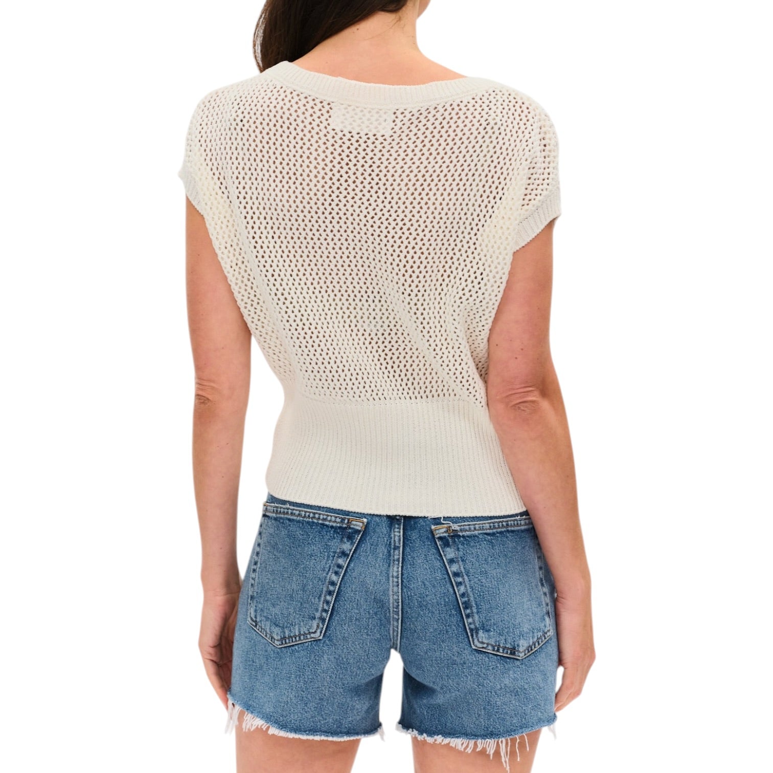 Person wearing a beige knit top and denim shorts on a white background