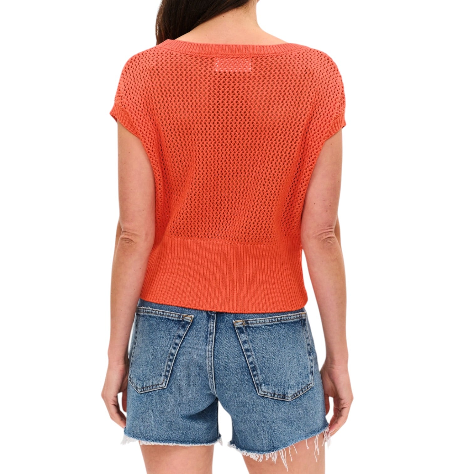 Person wearing an orange knit top and denim shorts on a white background