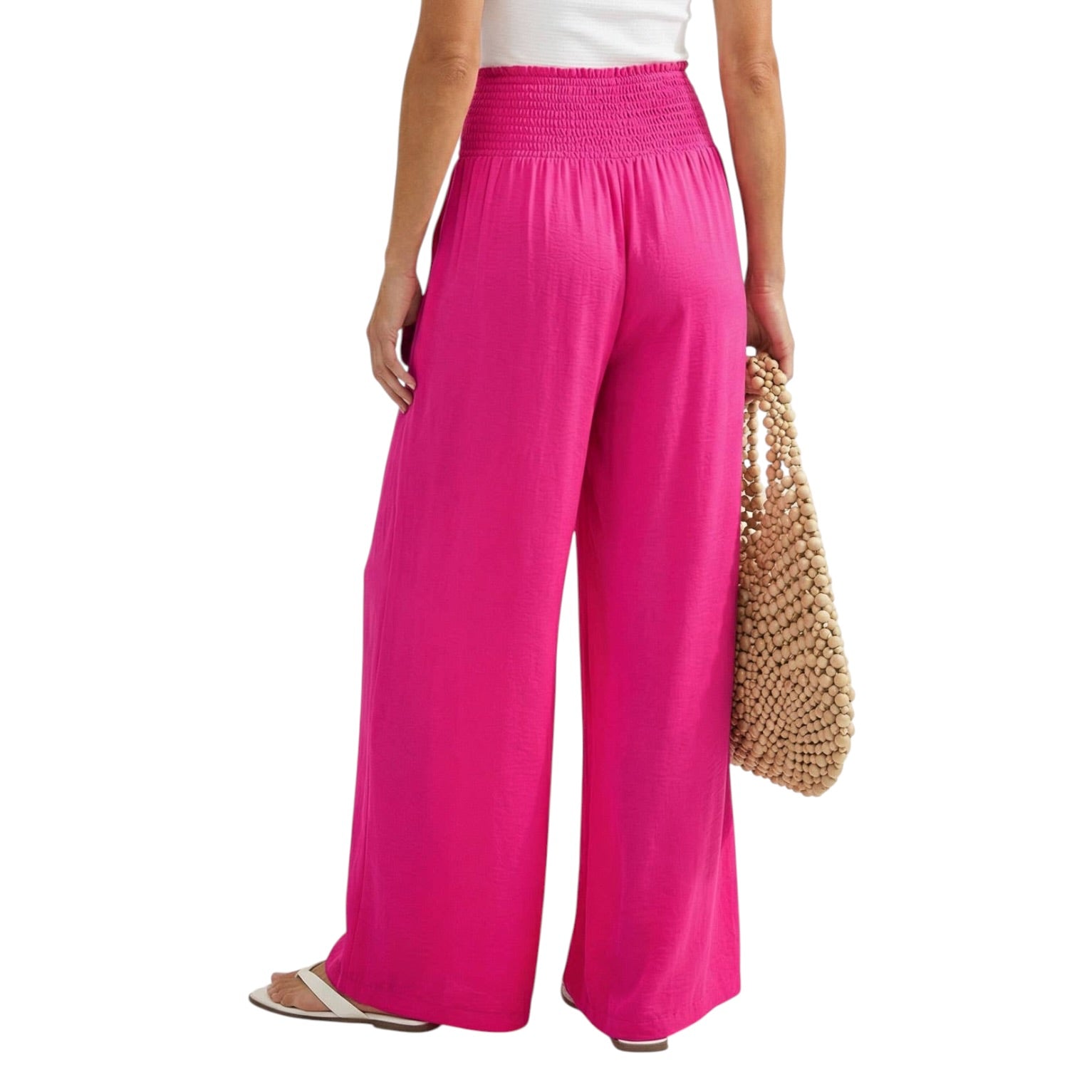 Person wearing bright pink wide-leg pants holding a beaded bag on a white background