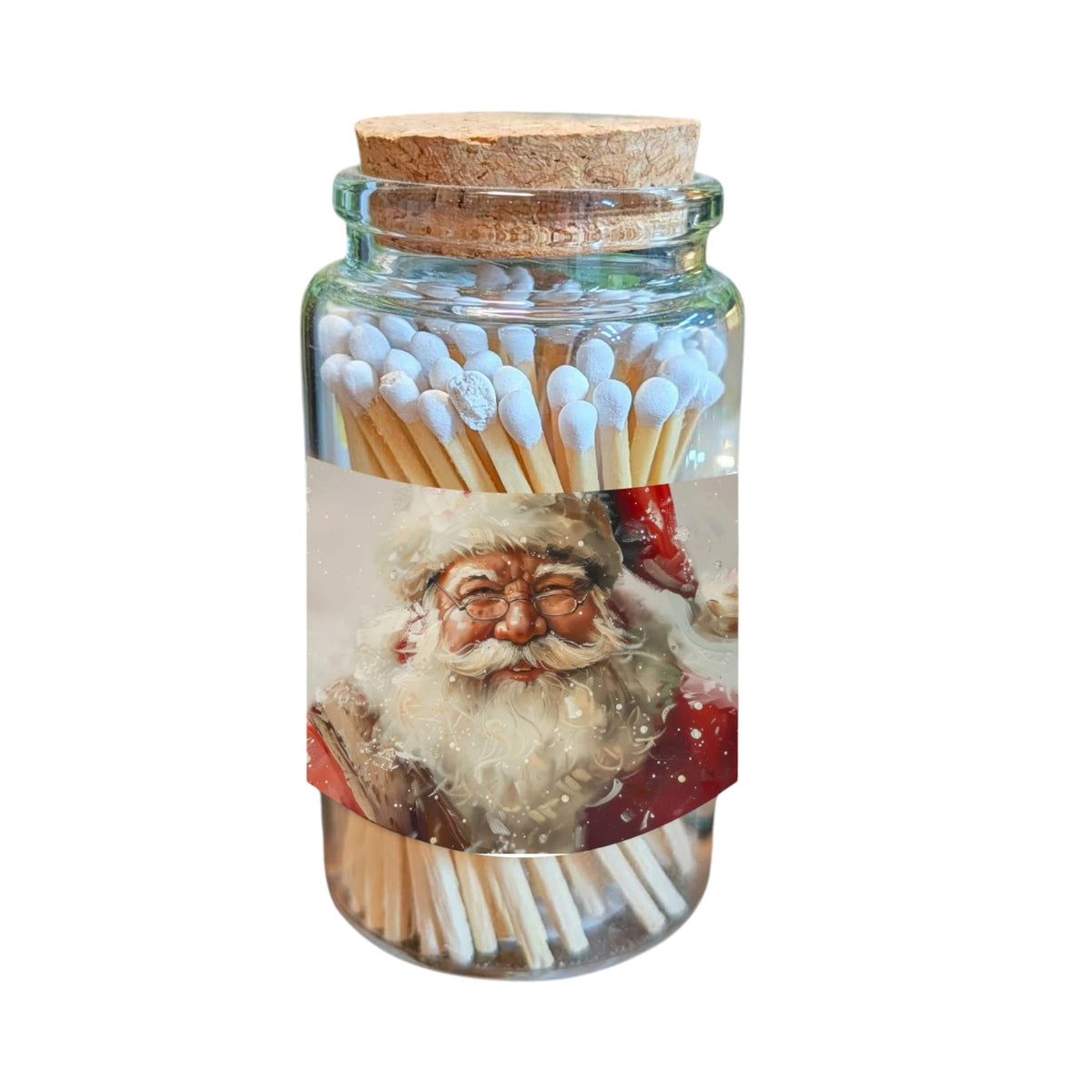 A clear glass jar with a cork lid, filled with wooden matches topped with white tips, and wrapped with a printed label showing a festive Santa Claus portrait. The jar is centered on a plain white background.