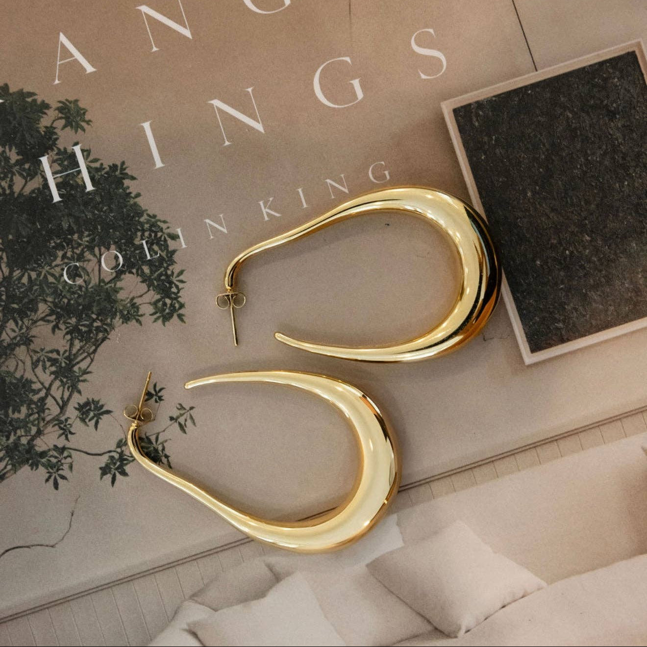 Gold hoop earrings on a surface with 'Hanging Things' book in the background