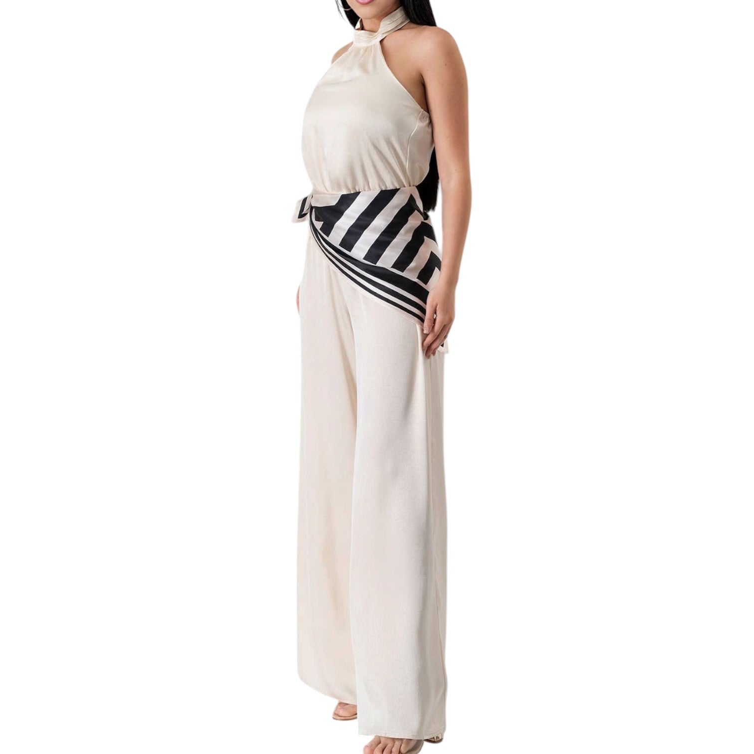 Woman wearing a white halter neck jumpsuit with black and white striped belt on a white background