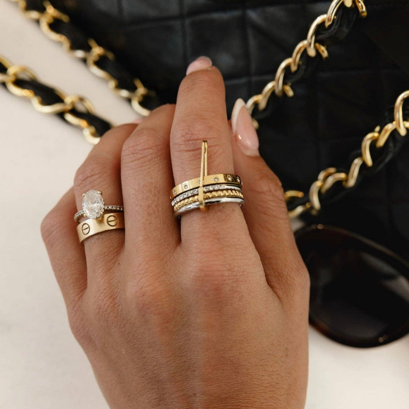 Hand wearing stacked gold rings with a black quilted handbag in the background