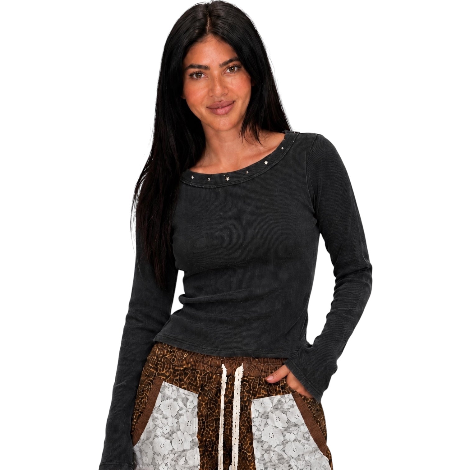 A woman modeling a dark charcoal gray long-sleeve top with a scoop neckline accented by small silver studs, paired with brown and white patterned pants, against a plain white background.