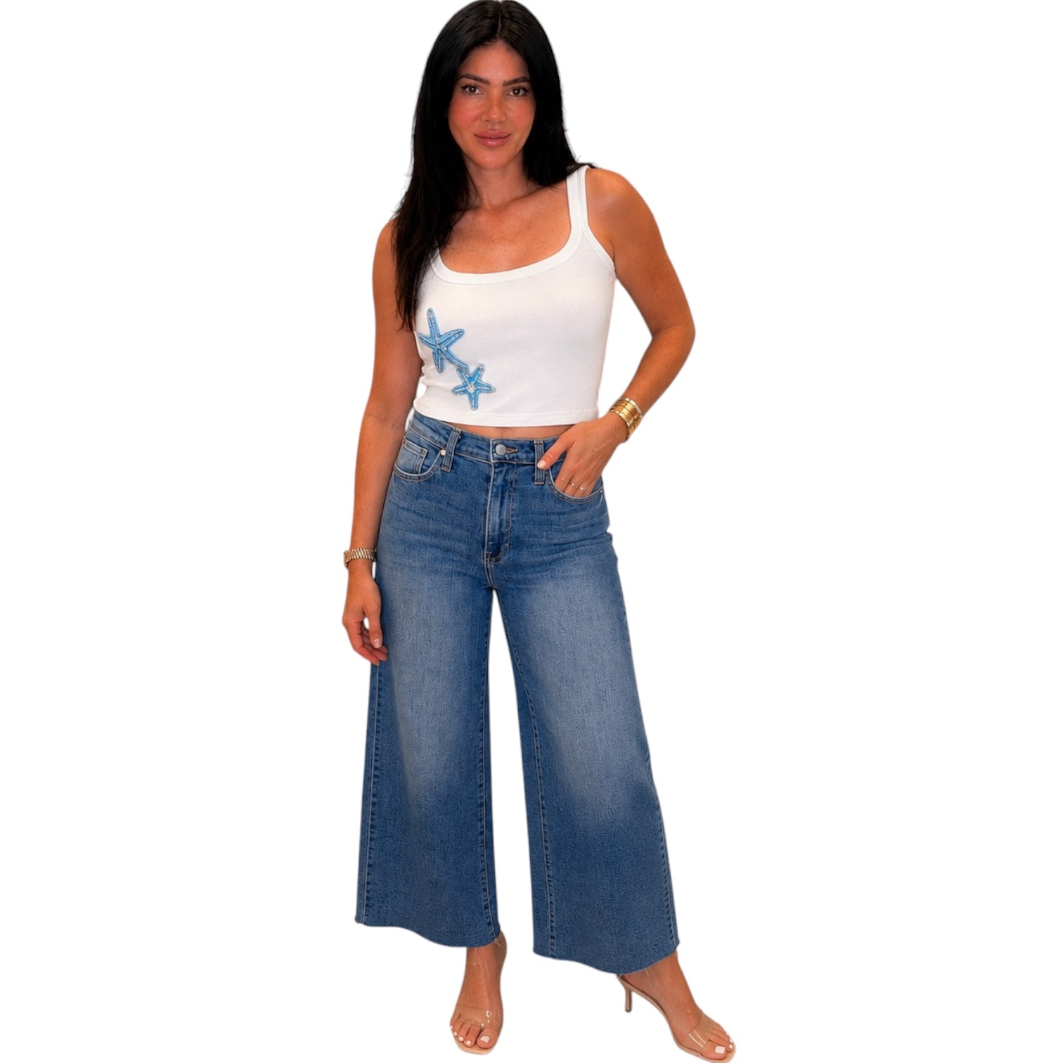 Woman wearing a white tank top with blue designs and blue jeans on a white background
