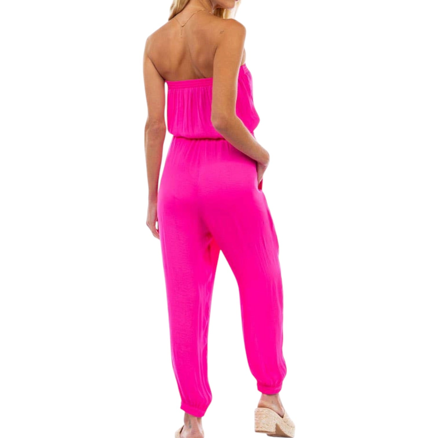 Woman wearing a bright pink strapless jumpsuit on a white background