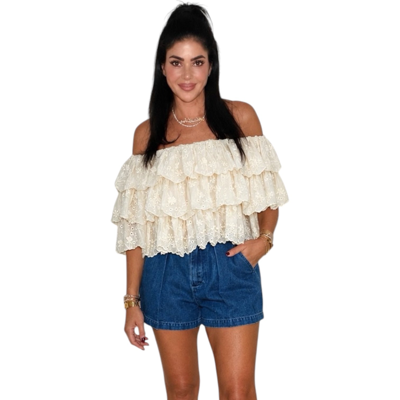 Woman wearing a cream off-shoulder lace top and blue denim shorts on a white background