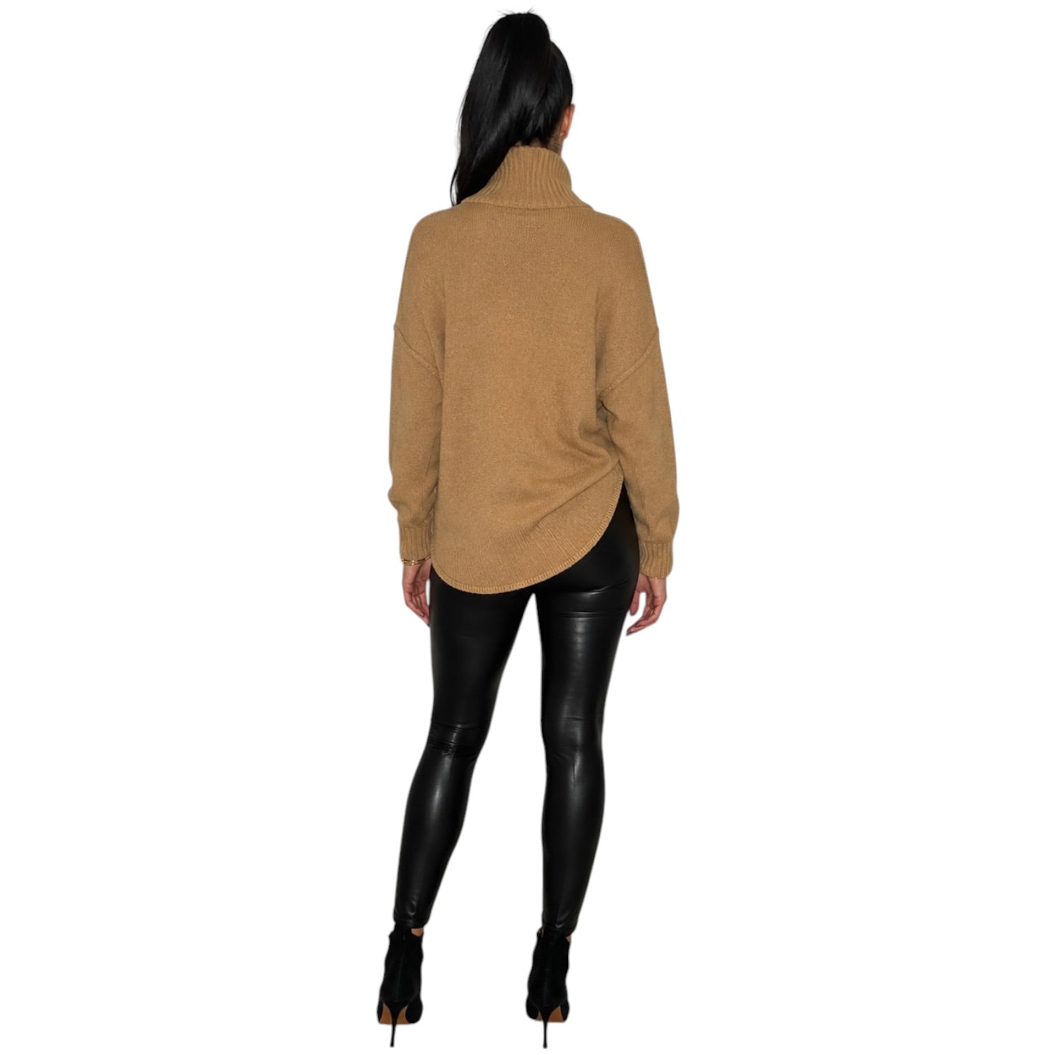 A woman shown from the back wearing a camel-colored turtleneck sweater, black faux-leather leggings, and black high-heeled boots against a plain white background.