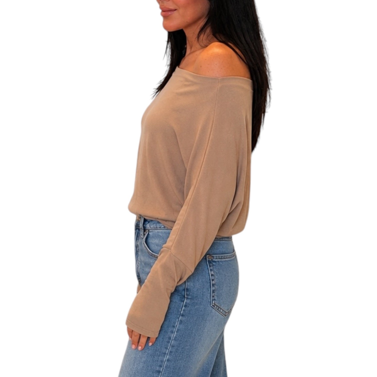 A woman shown in side profile wearing a beige off-the-shoulder long-sleeve top and blue jeans against a plain white background.